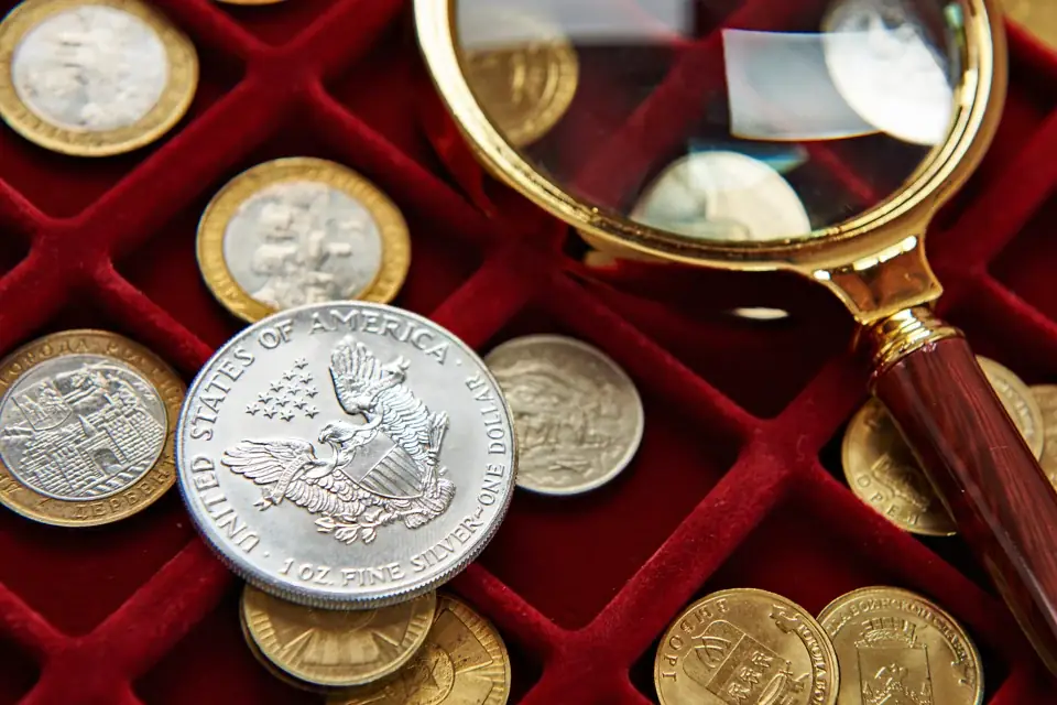 Coins laid out in a red velvet tray with a brass magnifying glass beside them
