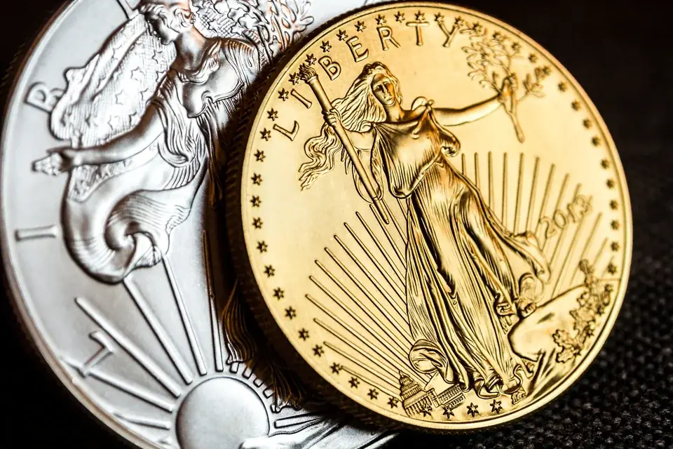Close view of a gold American Eagle leaning on a silver Eagle, both resting on dark fabric