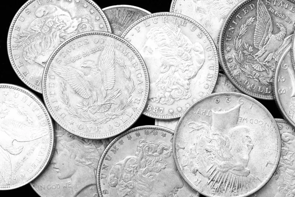 A heap of Morgan and Peace silver dollars in black and white